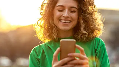 A woman standing outside while smiling at her phone 