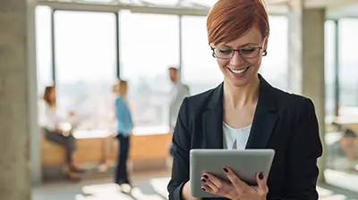 Woman in business attire smiling while using tablet.