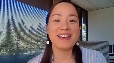 A webcam photo of a woman smiling at the camera while sitting in her office 
