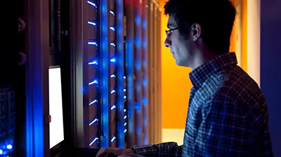 A man looking at a laptop in a server room